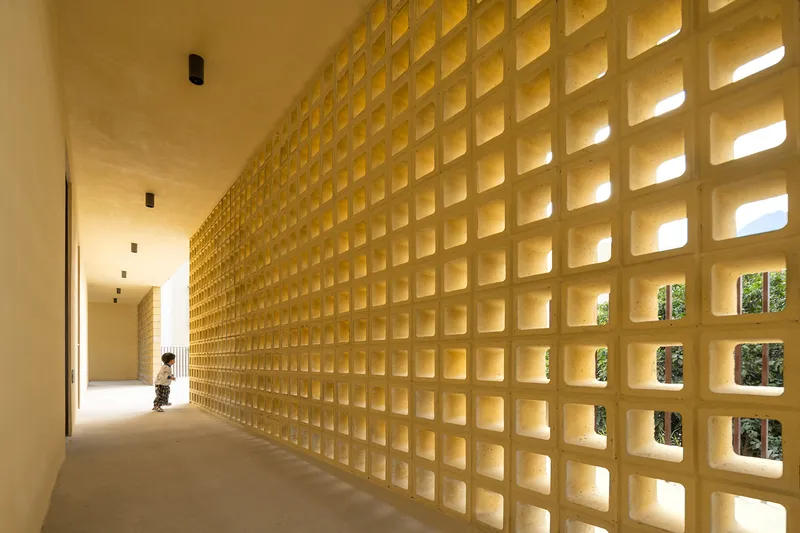 Long corridor with latticed concrete block wall filtering daylight as a child walks