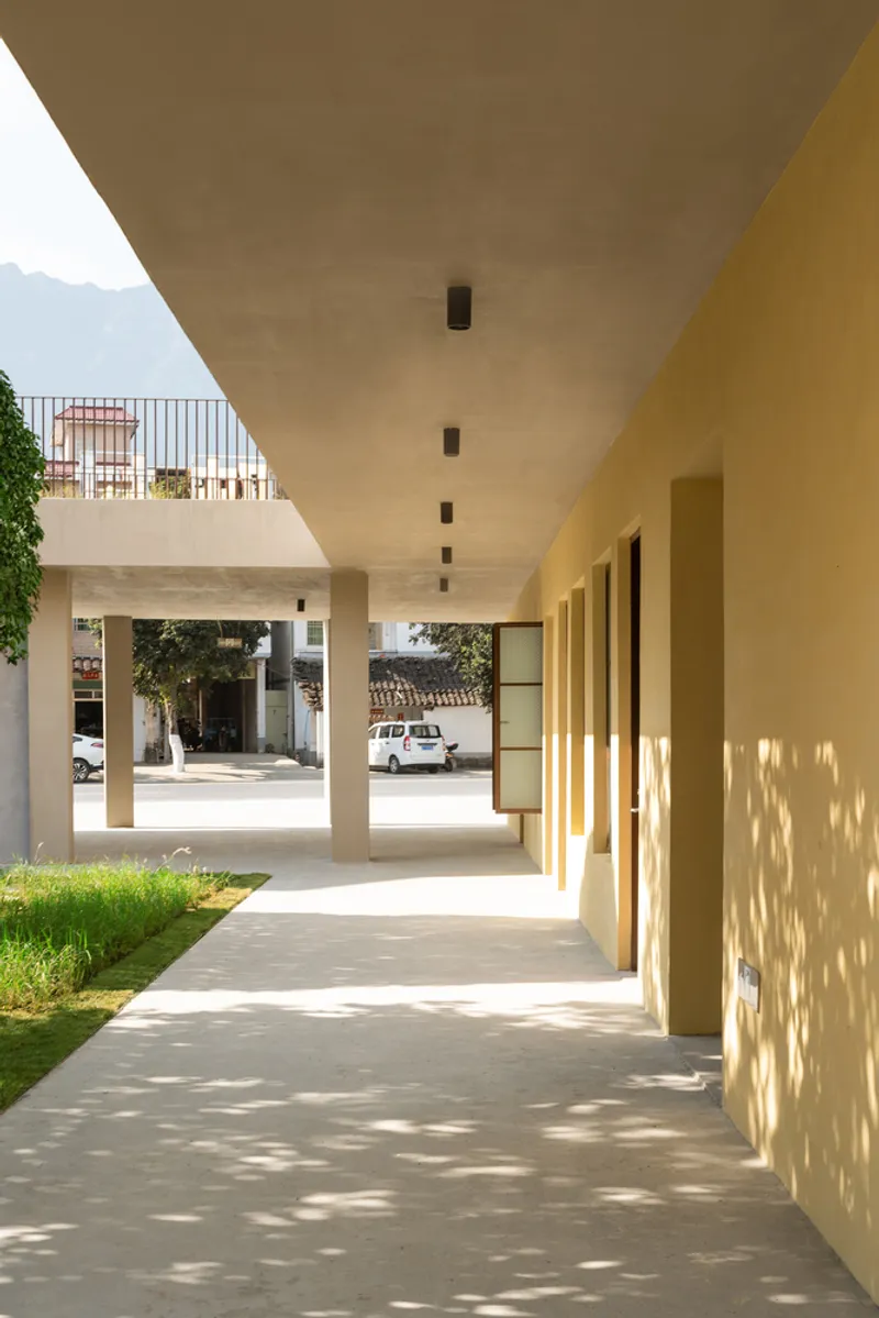 Colonnade with concrete ceiling and yellow walls casting dappled shadows onto the paved floor