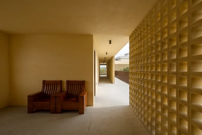 Covered corridor with textured yellow block wall and two dark wood chairs in afternoon light