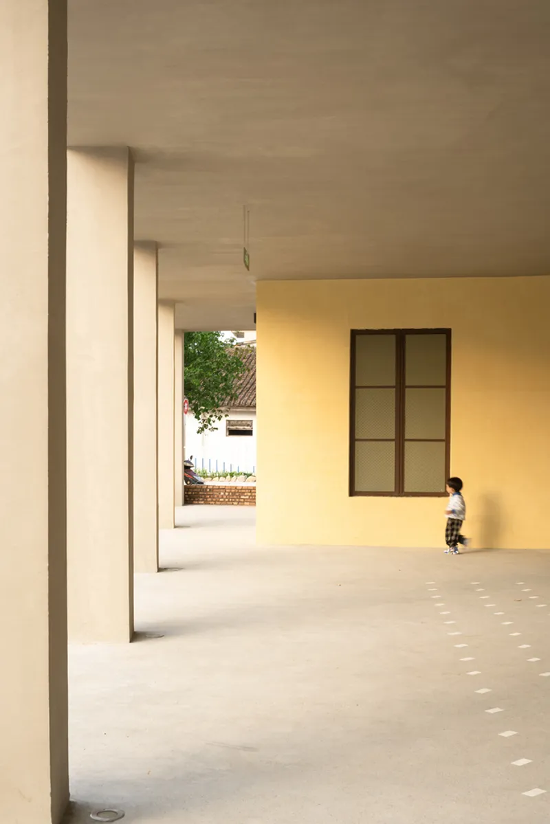 Covered courtyard with repeating columns and a child running across dappled light on concrete