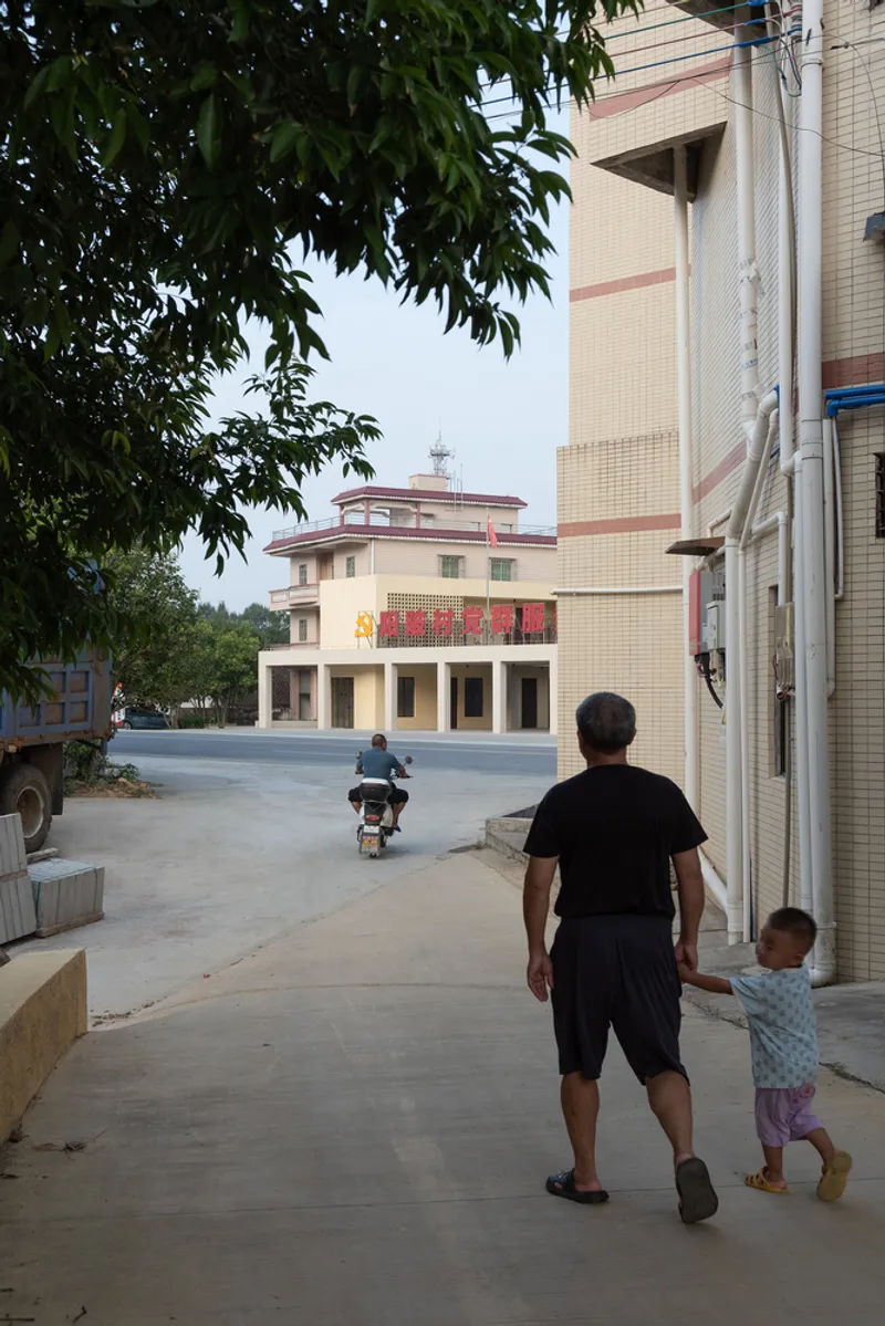 Street view with father and child walking toward an ochre colonnade building under overcast sky