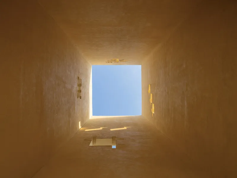 Upward view through a square light shaft with ochre rendered walls illuminated by daylight