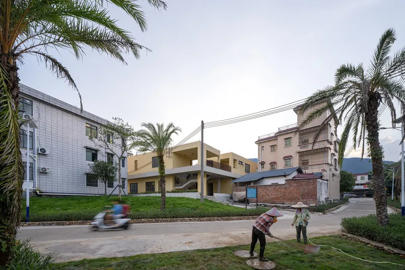 Terraced building with horizontal roof planes viewed from the road as a worker waters grass