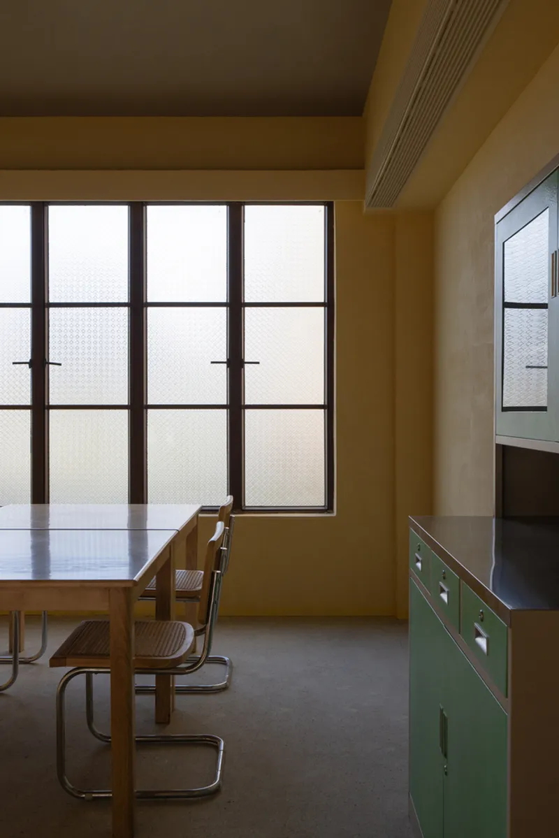 Interior dining room with translucent gridded window panels and green metal cabinetry under warm overhead lighting