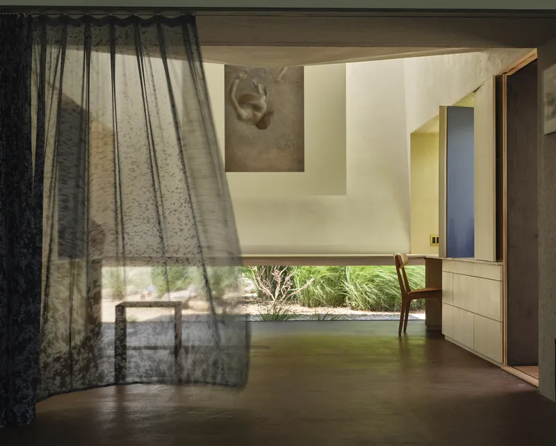 Sheer curtain filtering daylight across polished concrete floor with view to courtyard garden beyond