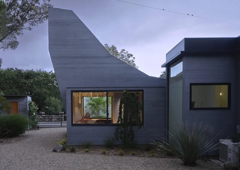 Exterior view of the angled concrete volume with corner window framing interior lounge at twilight