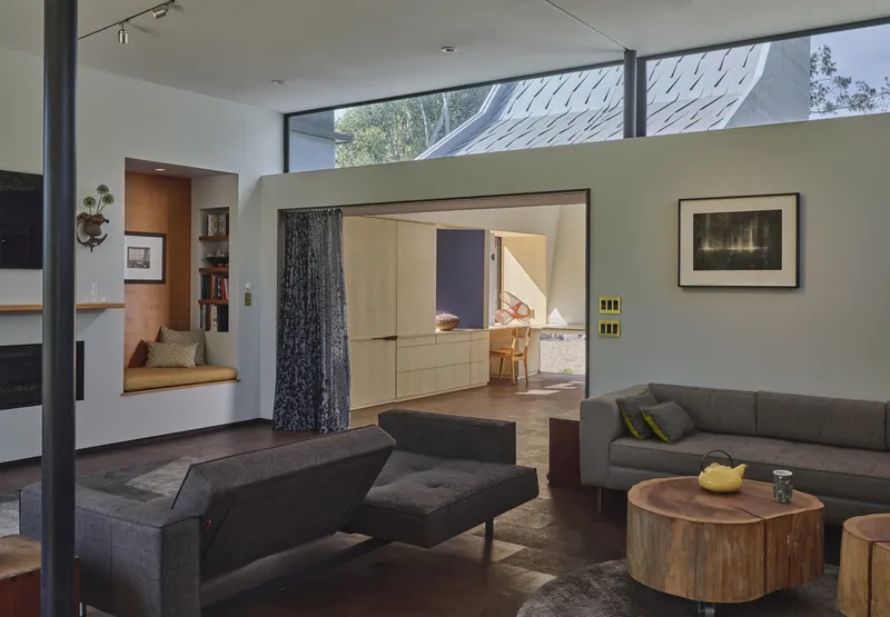 Living room with clerestory windows, built-in window seat, and framed opening to adjacent wood-clad space