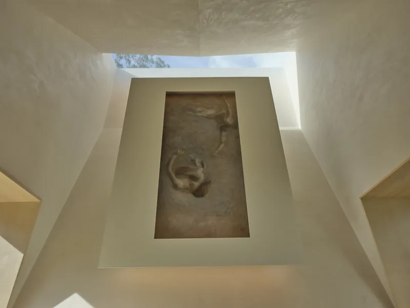 Upward view through a rectangular skylight framed by angled plaster walls with a fresco panel insert