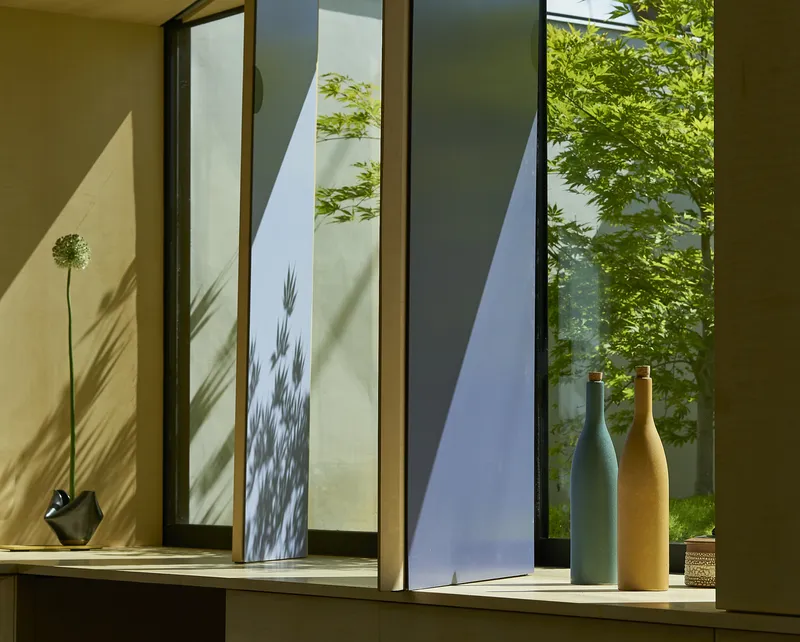 Interior window sill with ceramic vases casting shadows beside framed views of a courtyard tree