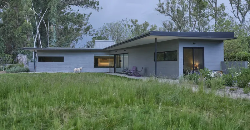 Single-story volume with low-pitched roofline set in tall grasses under an overcast evening sky