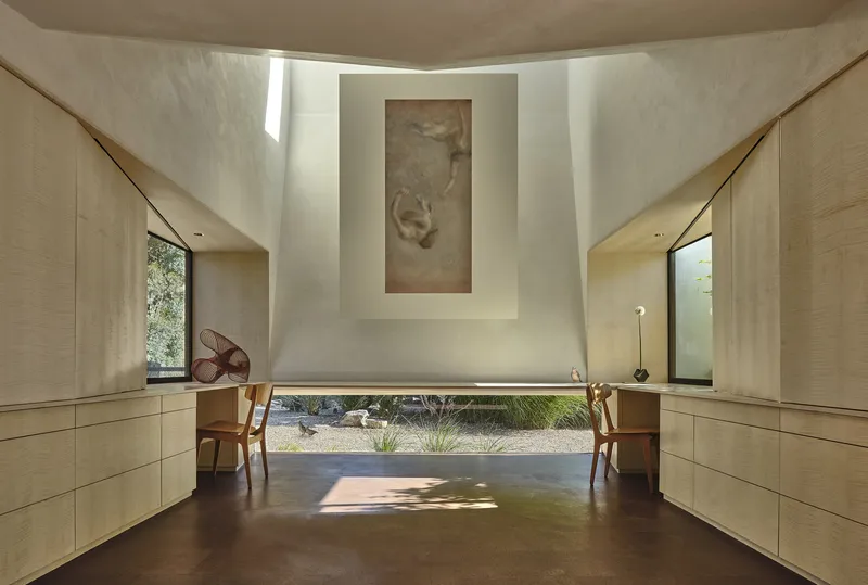 Double-height space with light wood cabinetry, recessed artwork niche, and view to planted gravel courtyard