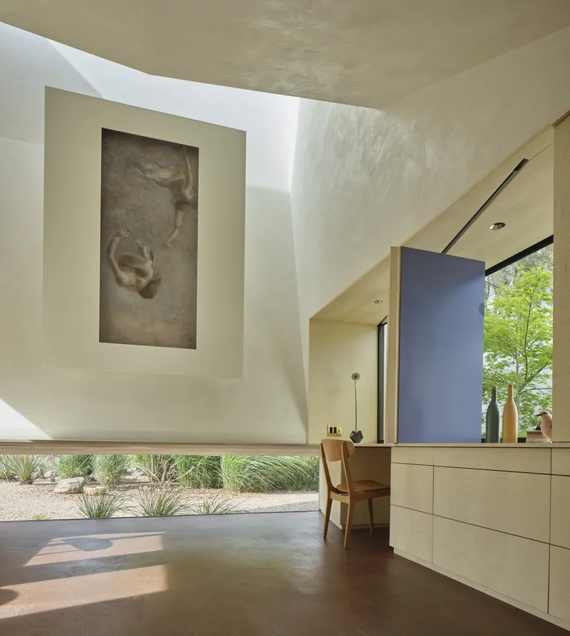 Interior corner showing curved ceiling plane, artwork niche, and built-in desk illuminated by afternoon sun
