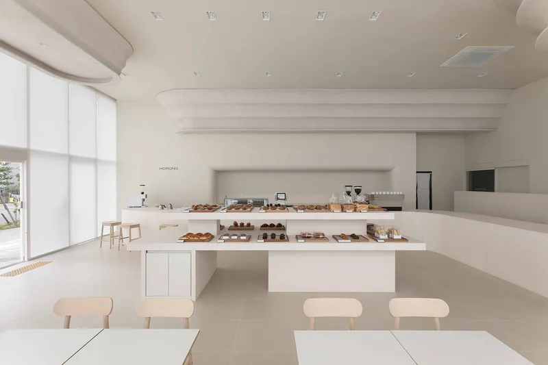 White bakery counter displaying bread and pastries beneath stepped horizontal ceiling beams