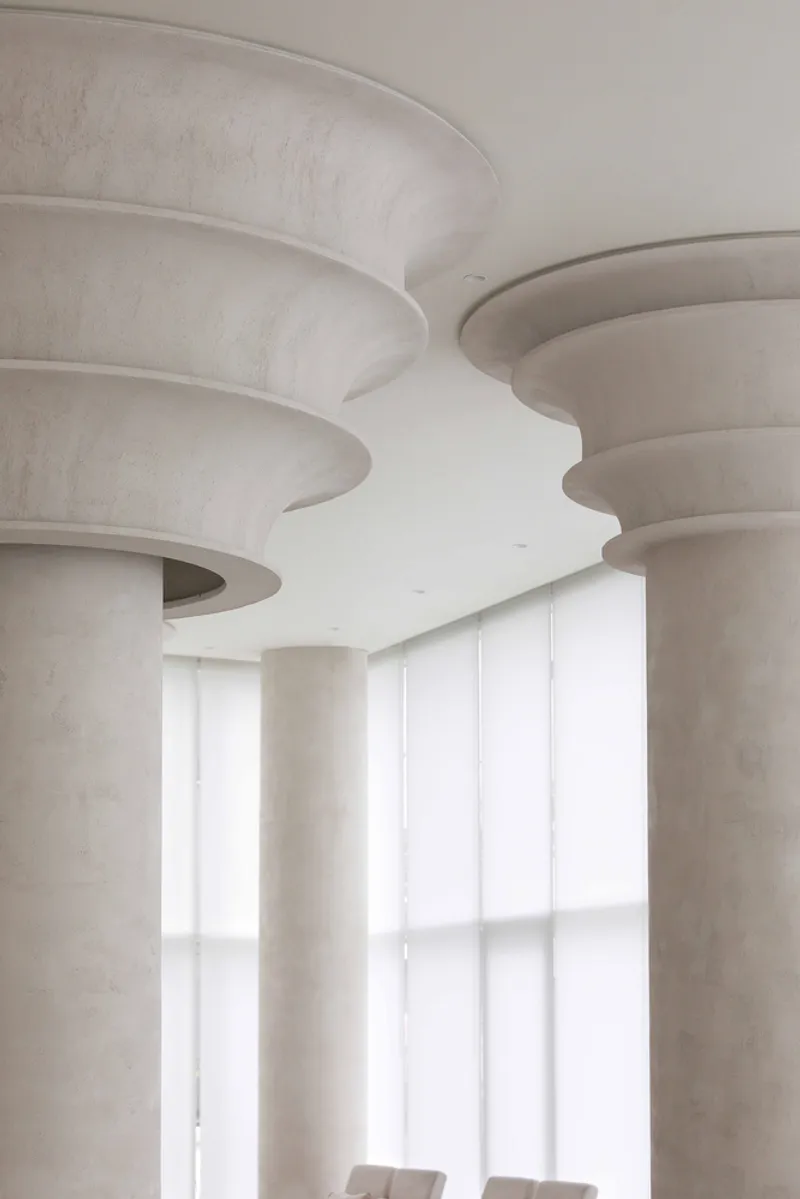 Close-up of stepped circular column capitals meeting the ceiling near diffused window light
