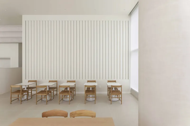 Row of timber chairs and tables against a vertical white slat wall partition