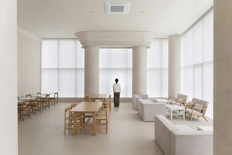 Interior room with a single person standing between white columns beneath floor-to-ceiling translucent window panels
