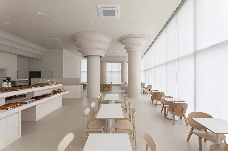 Bakery cafe interior with white display counter and timber seating under cylindrical columns with ringed capitals