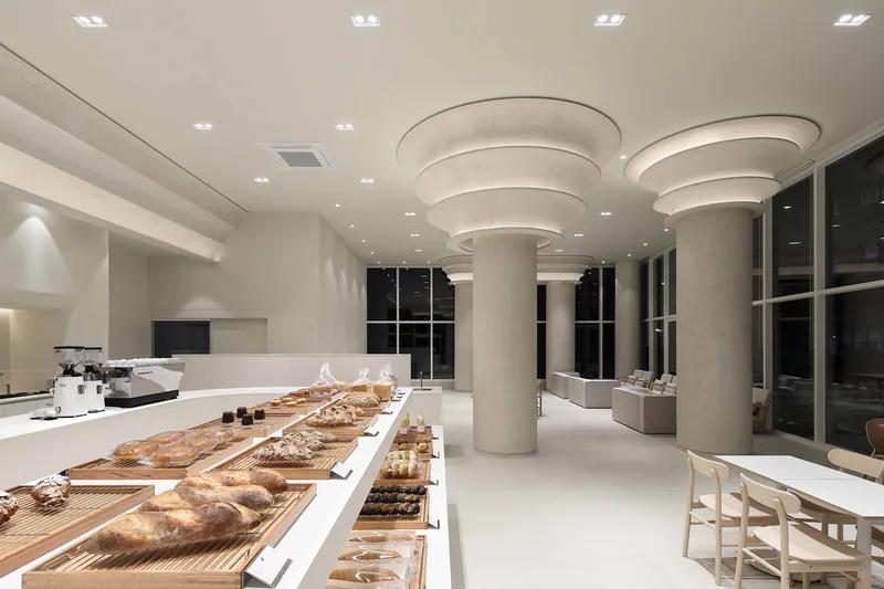 Interior of a bakery with tiered circular ceiling elements above a long counter displaying bread and pastries