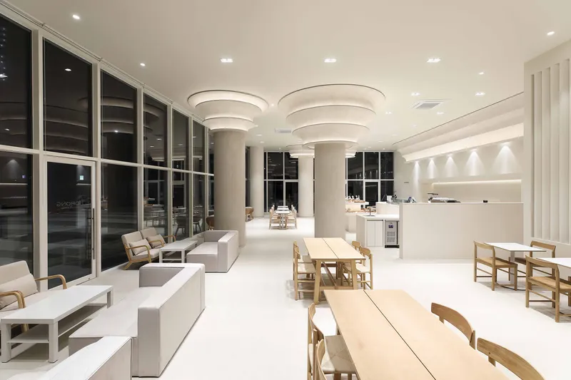 Evening view of lounge space with tiered column capitals and full-height glazing overlooking the night