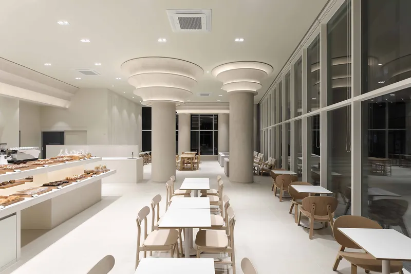 Cafe interior at night with illuminated stepped column capitals and large glazed facade reflecting darkness outside