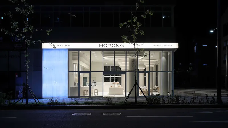 Street view of the fully glazed storefront illuminated at night with young trees flanking the entrance