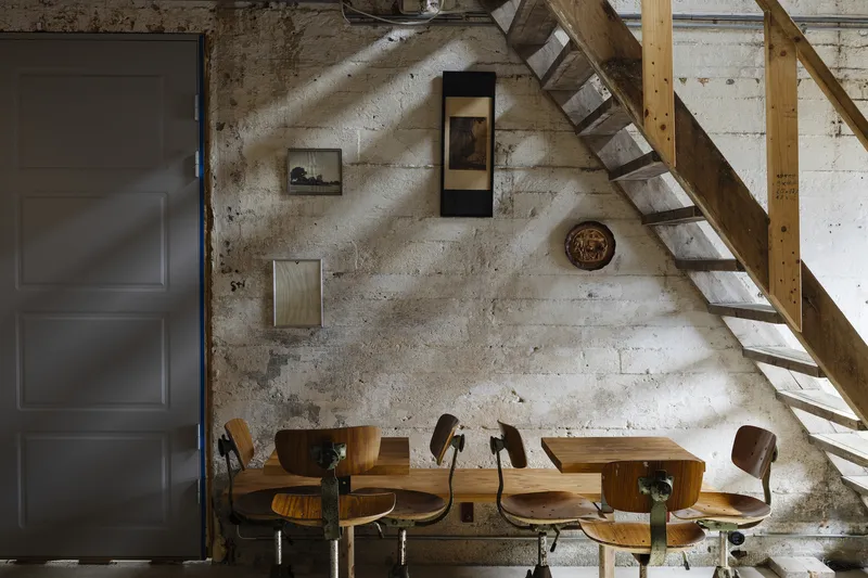Dining area with timber stairs ascending along a poured concrete wall in dappled sunlight