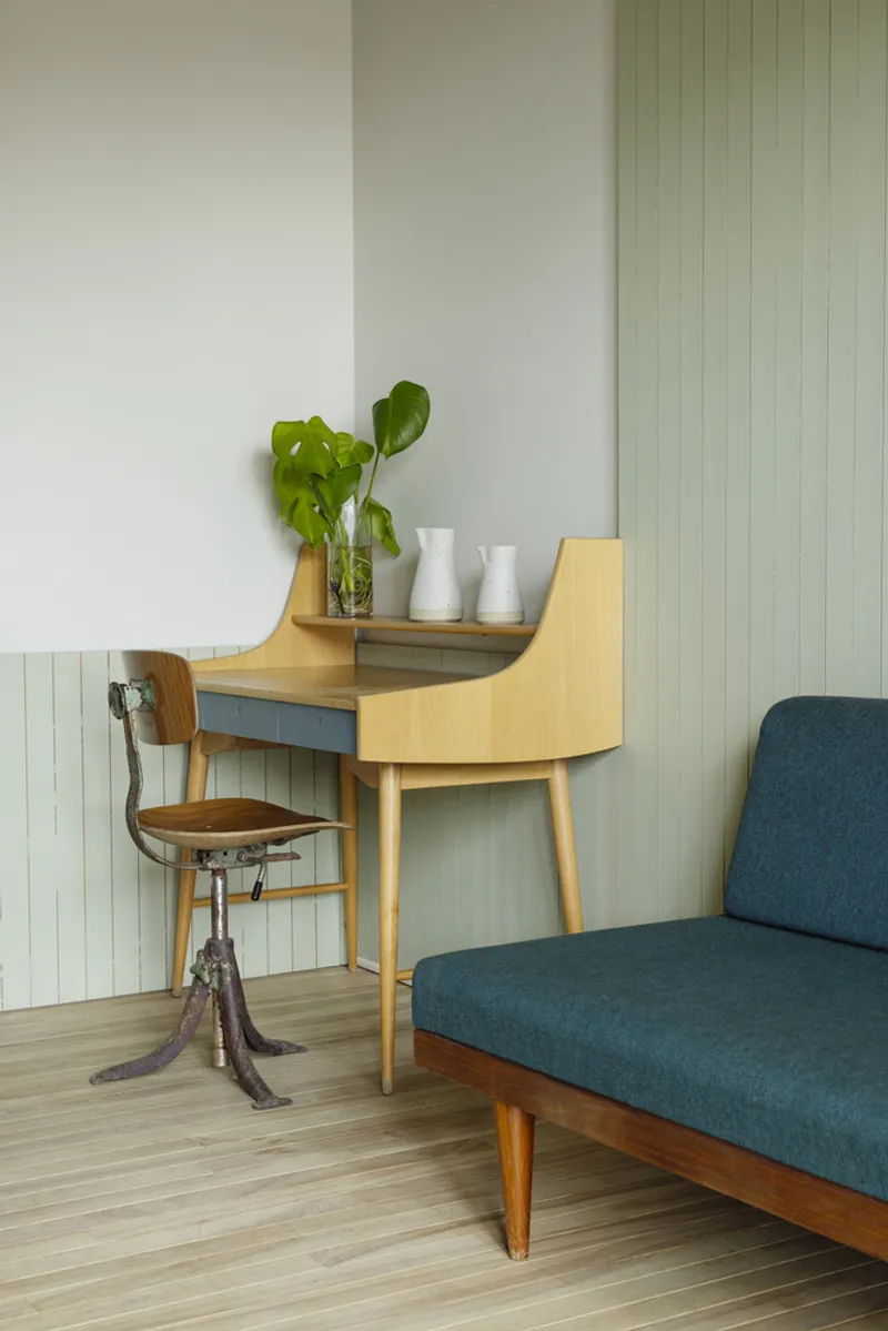 Corner desk with curved timber form and small chair against pale green vertical paneling