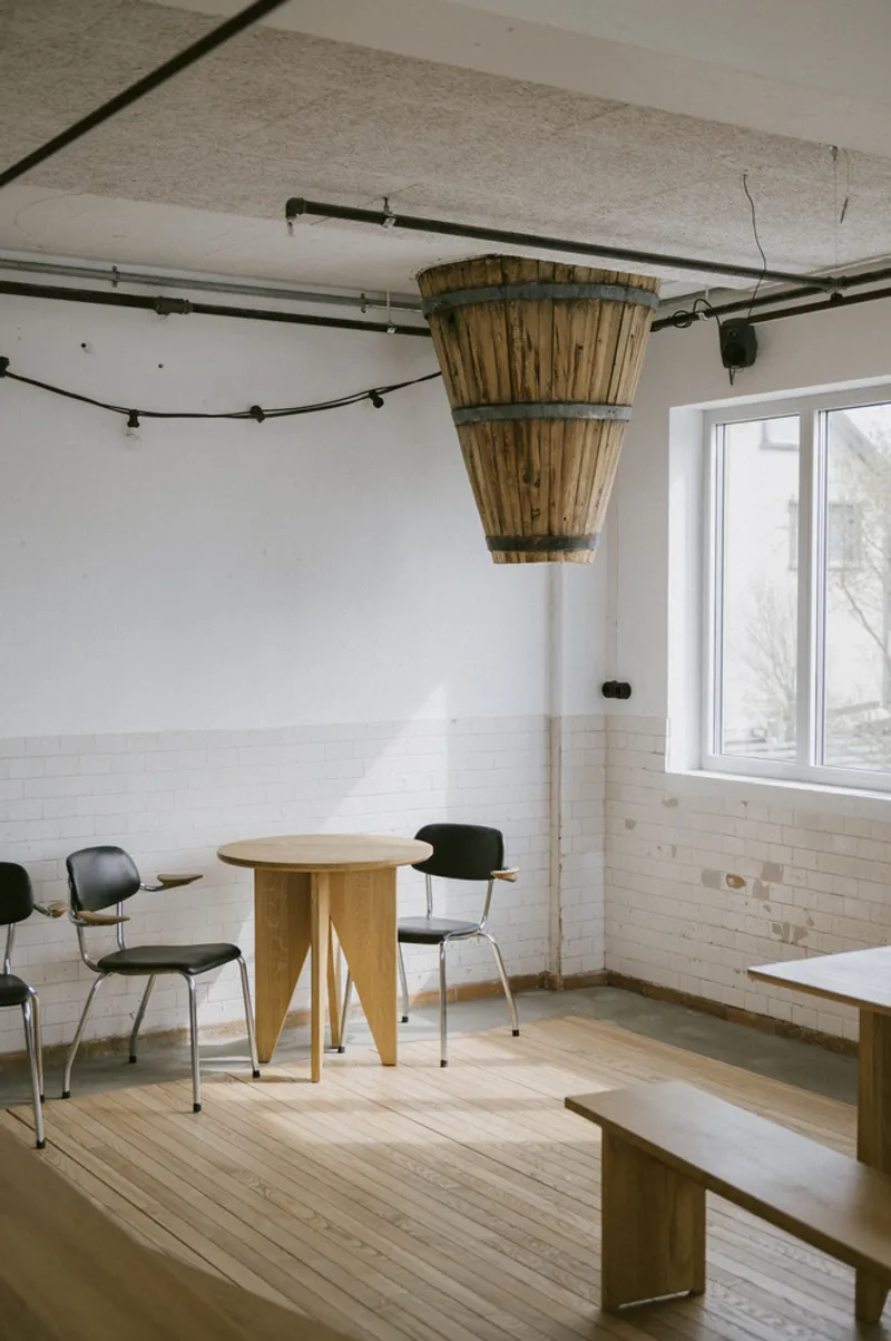 Common room with round timber table and suspended wicker basket lamp beneath exposed concrete ceiling