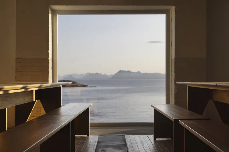 Timber benches flanking a large window framing distant mountains and calm water in afternoon light