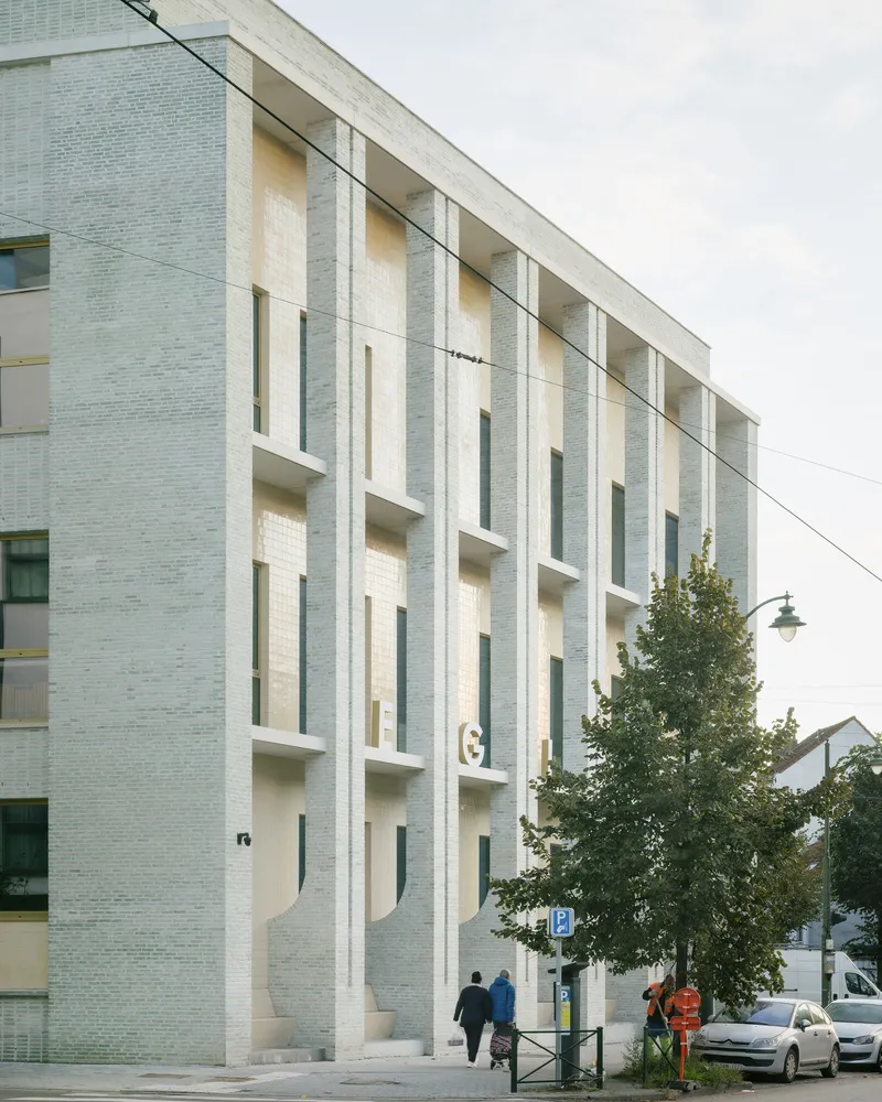 Street facade with pale brick and deeply recessed vertical window openings beneath an overcast sky