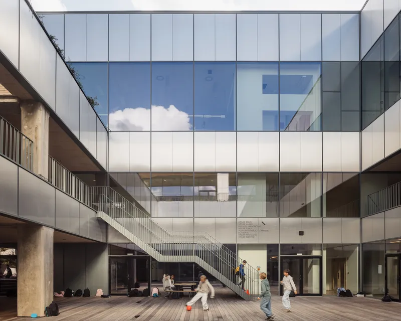 Interior courtyard with glass curtain wall, diagonal staircase, timber decking, and children playing