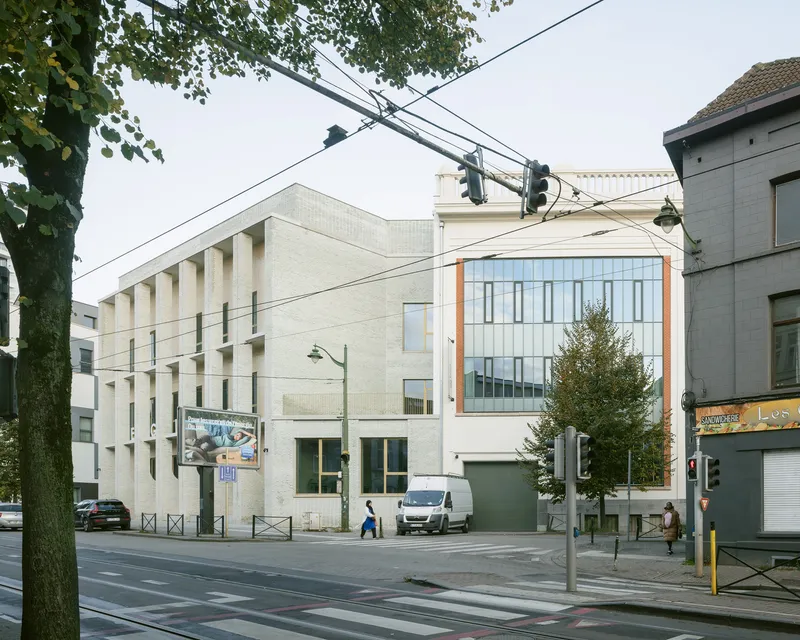 Street view showing pale brick facade with punched windows and power lines crossing the frame