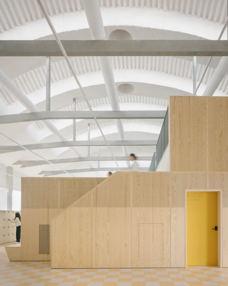 Interior space with plywood partition wall, yellow door, checkered floor, and exposed white steel trusses above