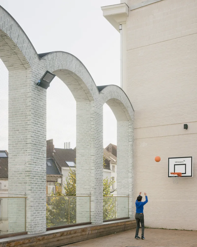 Courtyard view with pale brick arches and a person shooting a basketball at a mounted hoop
