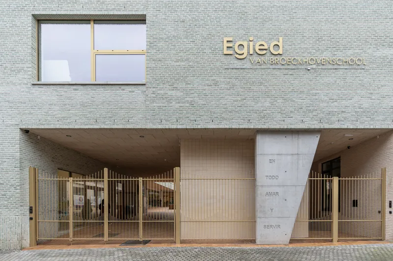 Entry facade with recessed loggia, brass lettering, vertical metal gates and inscribed concrete panel