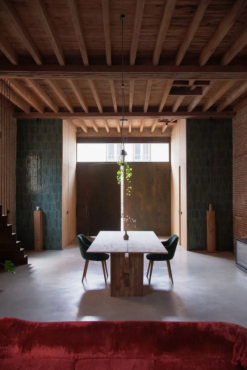 Dining area with exposed timber joists and green tile walls flanking a window with hanging plant