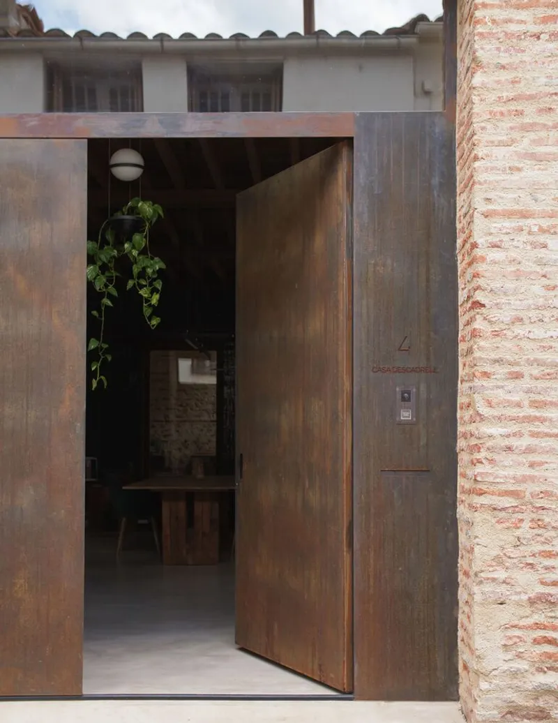 Weathered steel entry door set within a frame of recycled brick walls in daylight