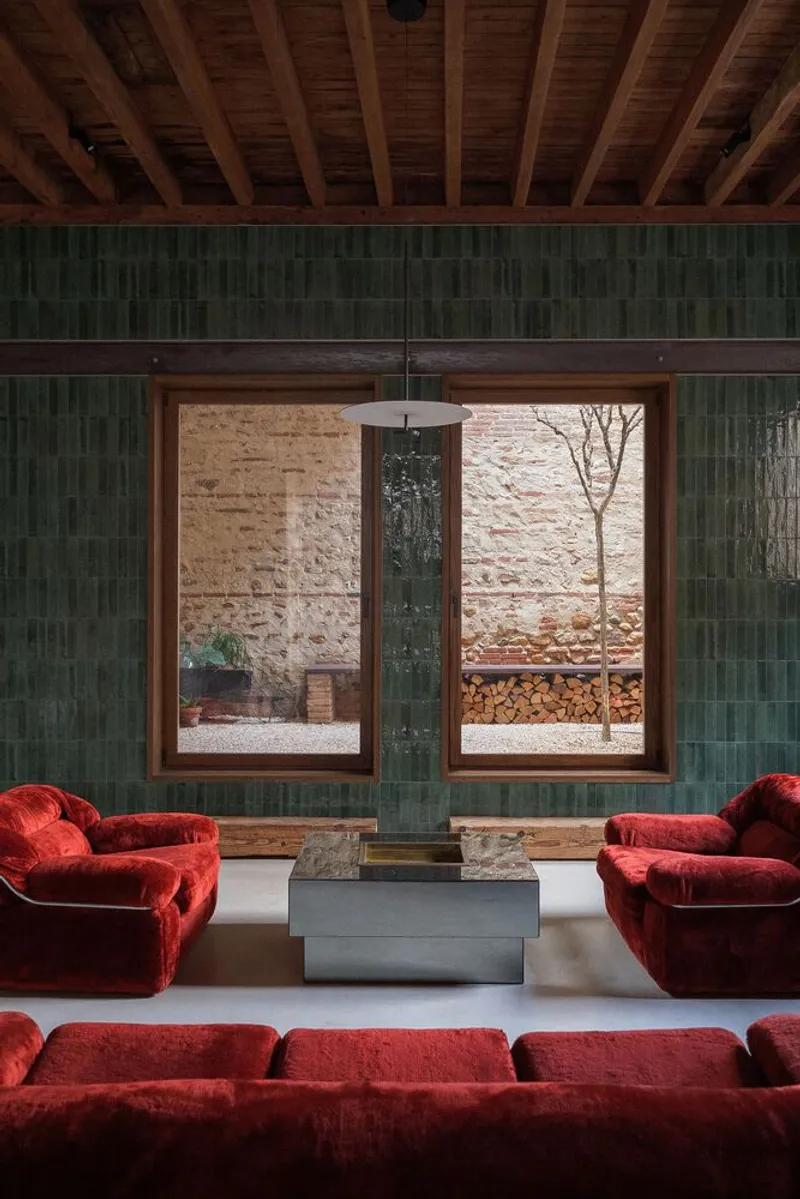 Living space with green tile column, timber window frames framing a courtyard view and firewood storage