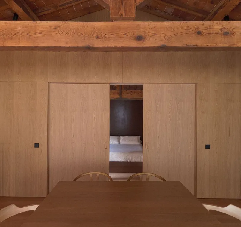 Interior with light oak sliding doors opening to a bedroom under an exposed timber beam ceiling