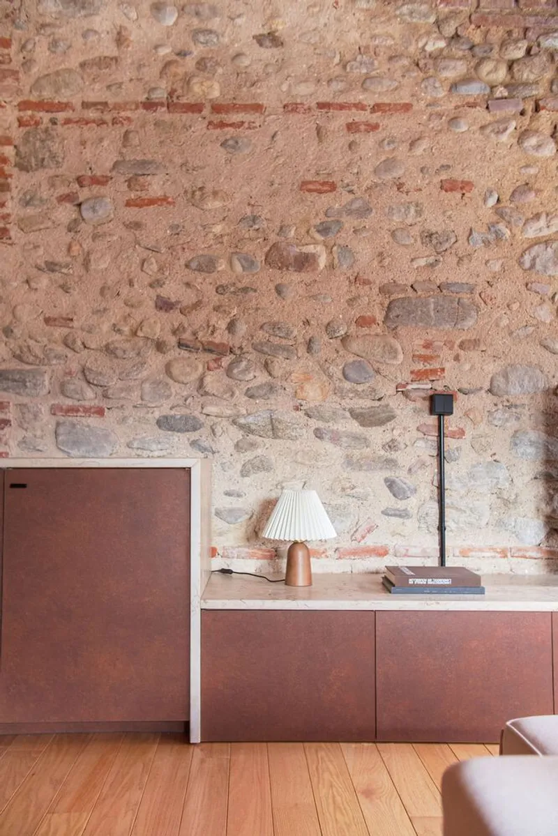 Copper-toned cabinet beneath a stone and brick wall with terracotta banding and table lamp