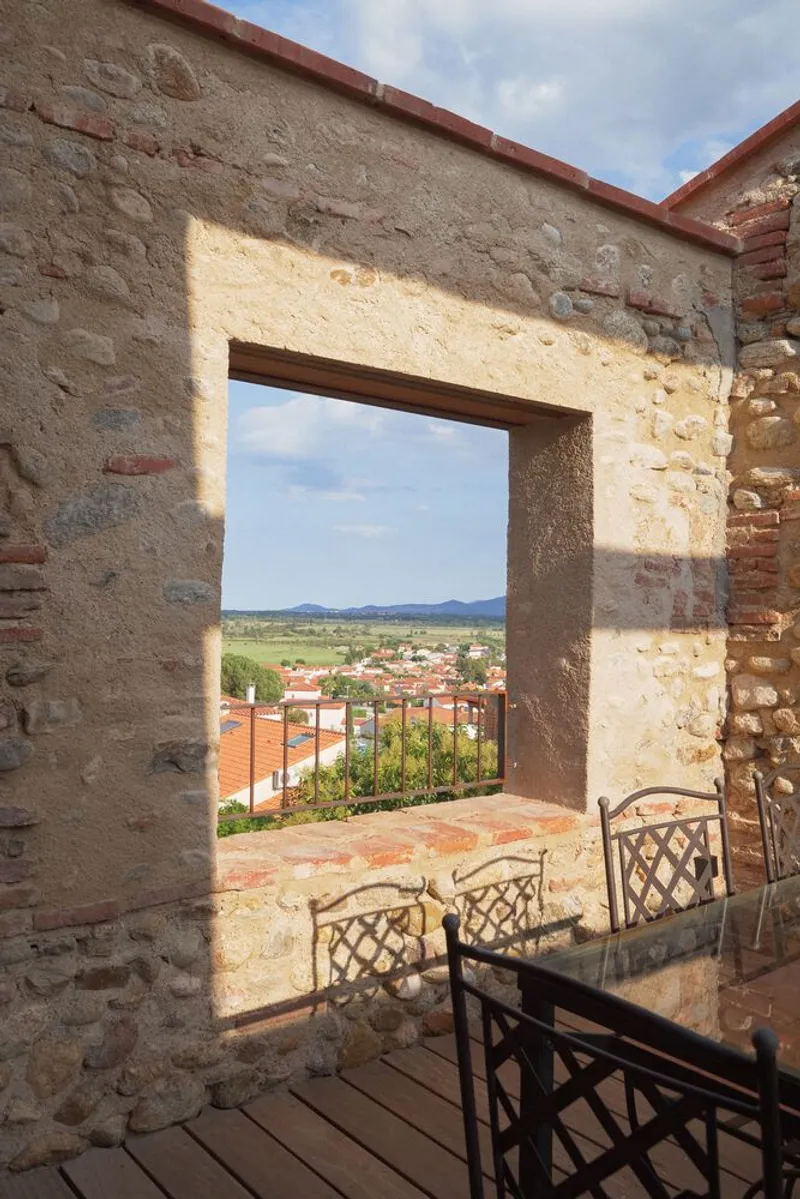 Stone and brick window opening framing views of terracotta rooftops and distant hills under bright sun