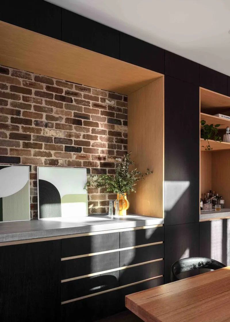 Kitchen with exposed brick wall framed by timber niche and black oak cabinetry with brass pulls
