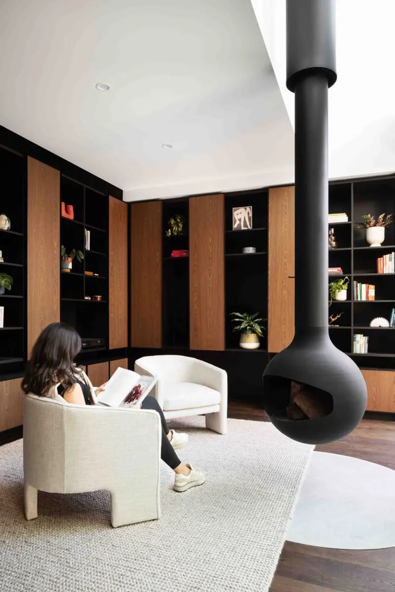 Reading room with suspended black fireplace and timber and black shelving wall with a seated figure