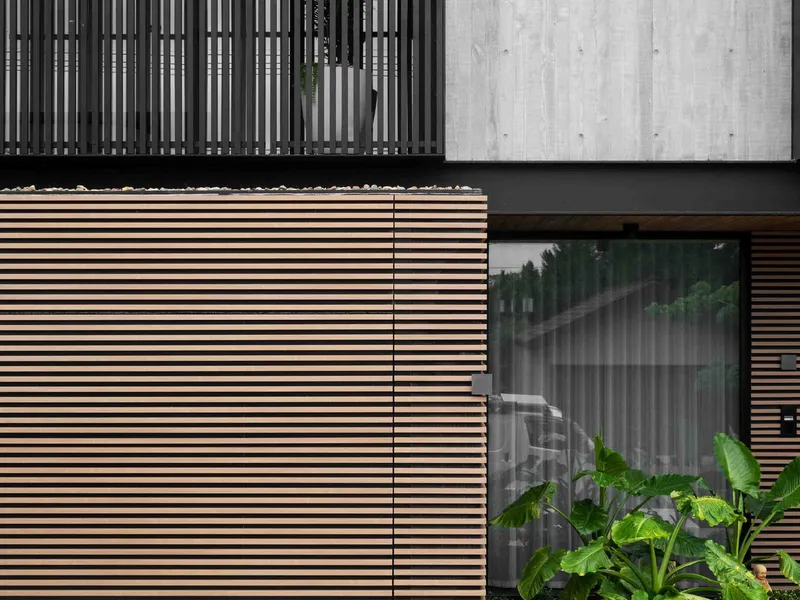 Close-up of horizontal timber slat cladding with glass window reflecting trees and tropical plantings below