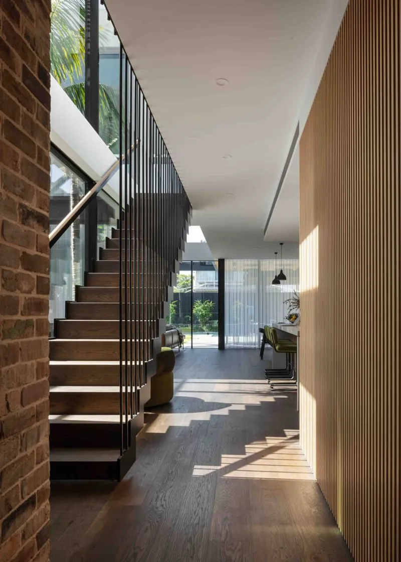 Entry hall with floating timber stair, vertical metal balustrade and slatted partition framing views to the garden