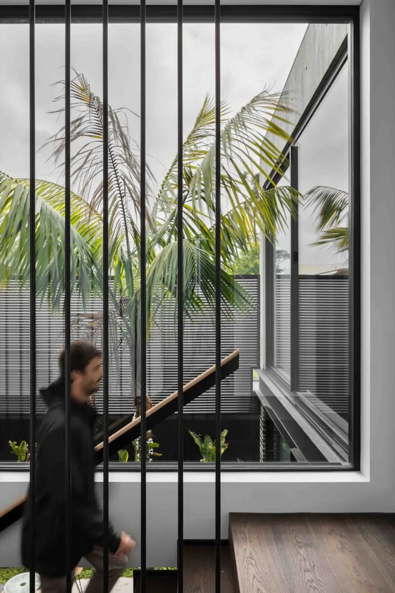 Interior view through vertical metal screen to courtyard palms as a figure descends the timber stair