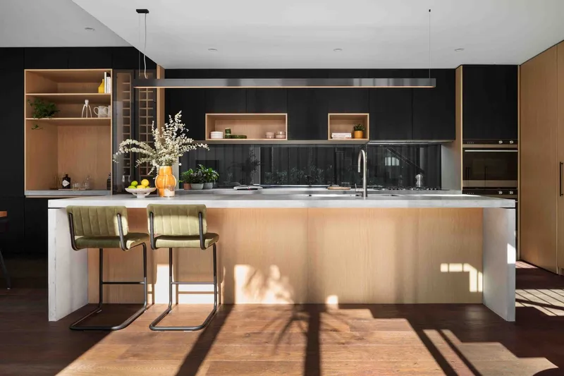Kitchen island with timber-clad base and black cabinetry casting long shadows across dark timber flooring