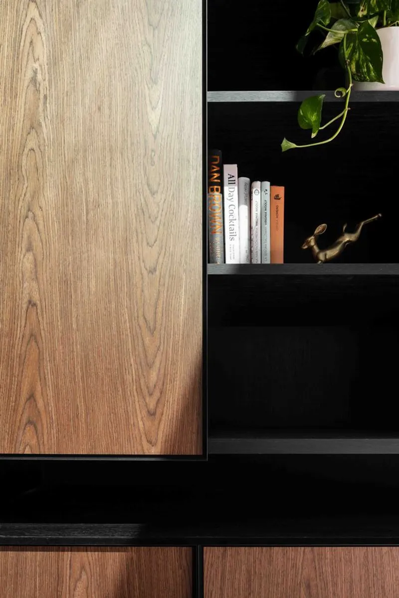 Detail of sliding timber cabinet door meeting black shelving with potted plant and books