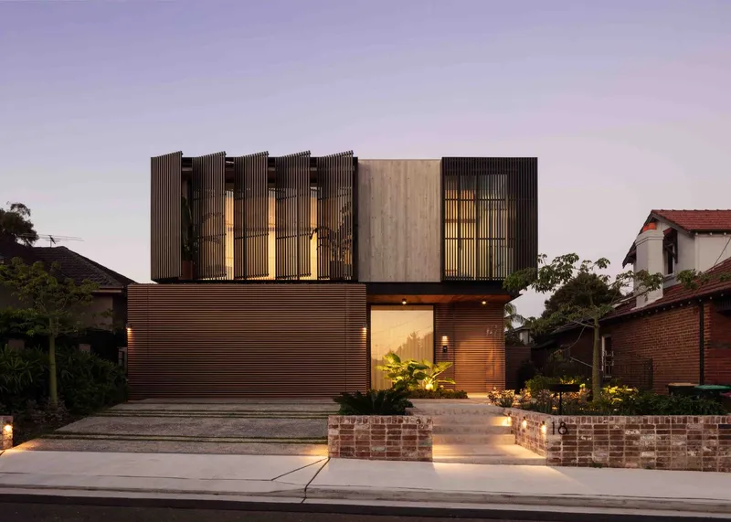 Street facade with corrugated metal cladding and vertical timber screens illuminated at dusk