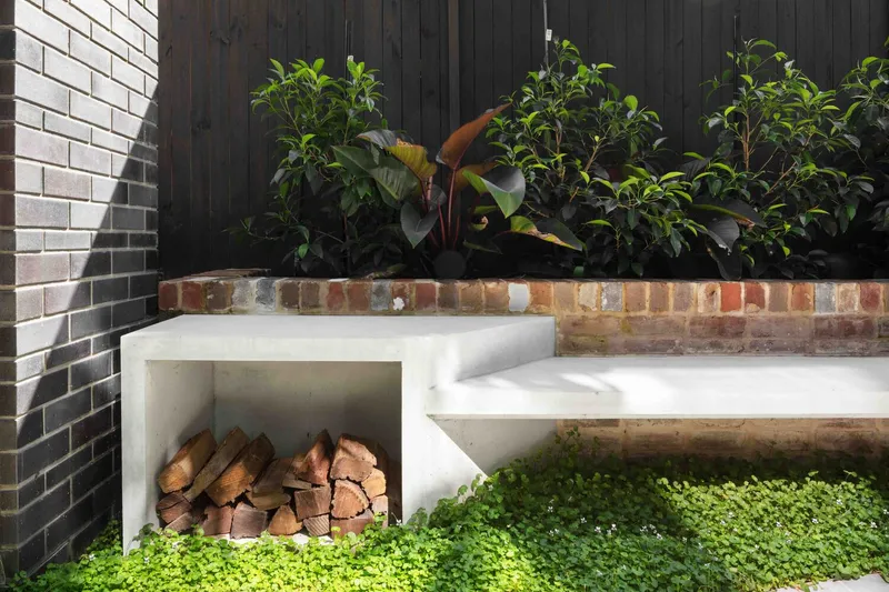 White concrete bench seat with integrated firewood storage and raised brick planter bed behind